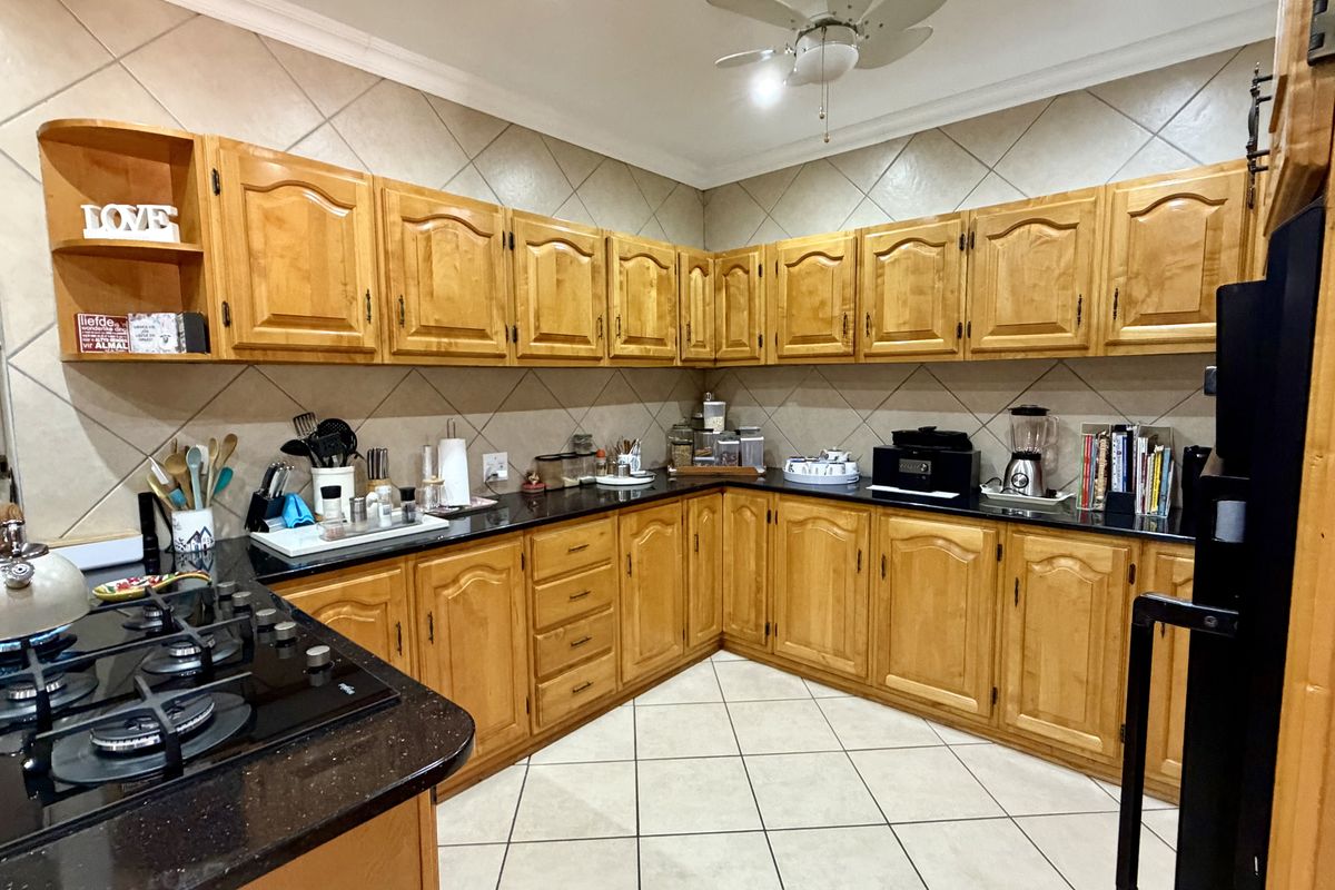 A functional kitchen featuring extensive wooden cabinetry, black granite countertops, a gas hob, and neutral tiled flooring with a classic backsplash.
