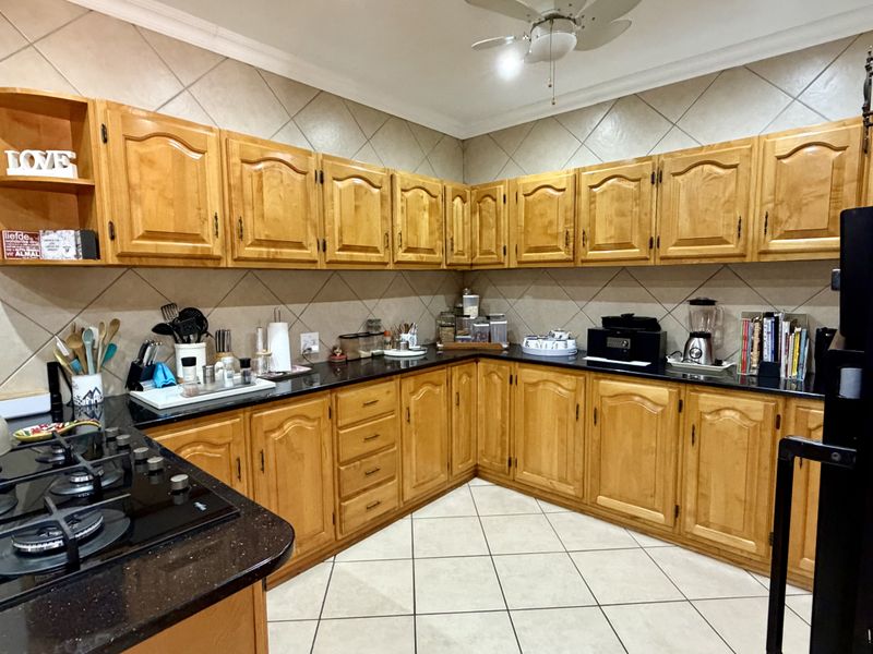 A functional kitchen featuring extensive wooden cabinetry, black granite countertops, a gas hob, and neutral tiled flooring with a classic backsplash.