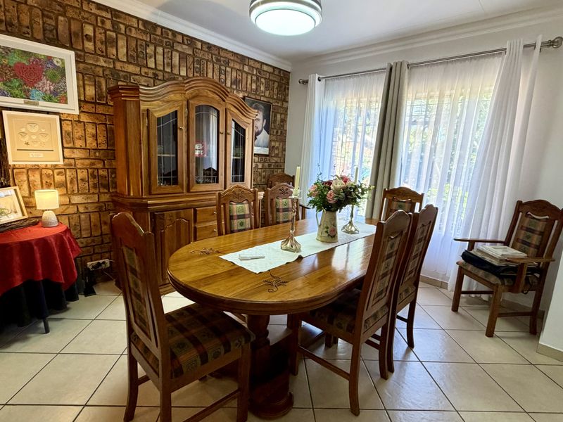 A dining room featuring an exposed brick feature wall, ceramic tiled flooring, and natural light through large windows with curtain rails.