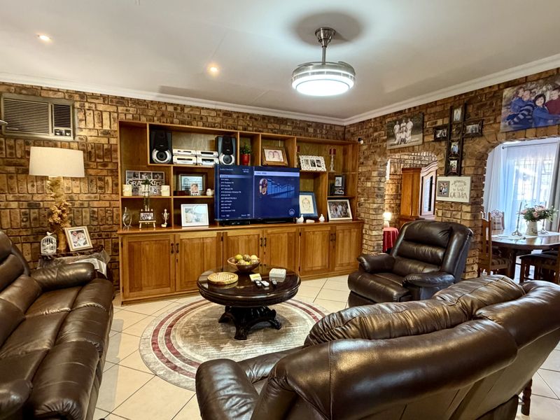 A spacious living room featuring distinctive exposed brick walls, custom built-in wooden cabinetry, and tiled flooring, creating a warm and traditional atmosphere.