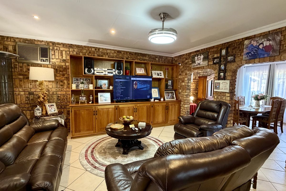 A spacious living room featuring distinctive exposed brick walls, custom built-in wooden cabinetry, and tiled flooring, creating a warm and traditional atmosphere.