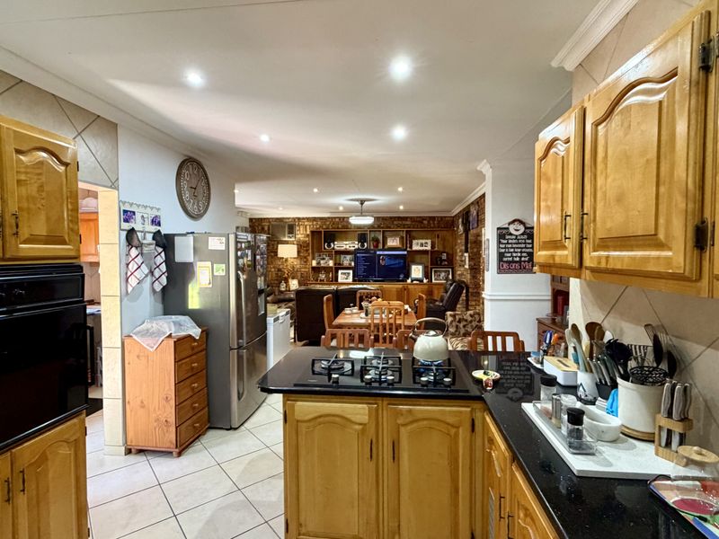 Open-plan kitchen and living area featuring wooden cabinetry, black granite countertops, gas hob, built-in oven, and an exposed brick feature wall.