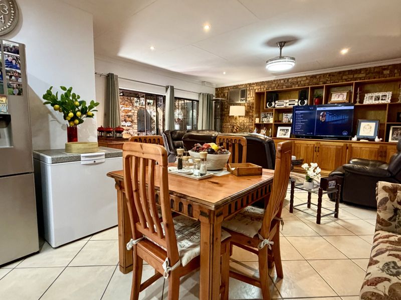 Spacious open-plan living and dining area featuring tiled floors, built-in wooden shelving, and an exposed brick feature wall.