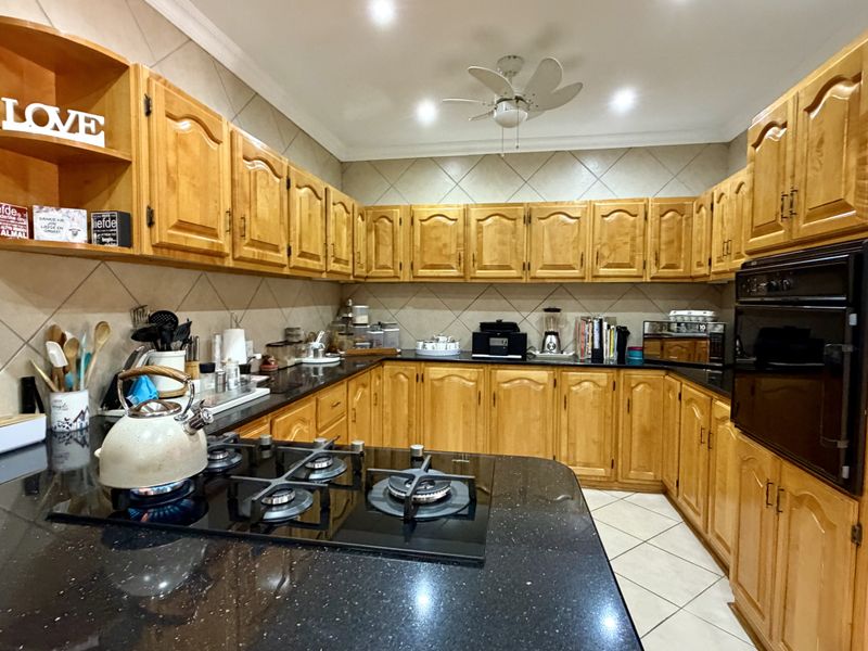 A functional kitchen featuring extensive wooden cabinetry, black granite countertops, a gas hob, and a built-in oven with a tiled backsplash.