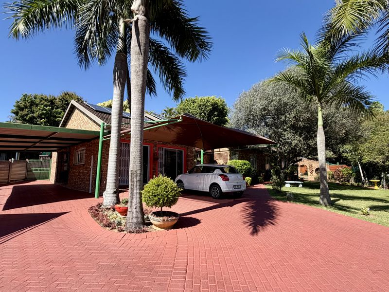 Front exterior view of the property featuring extensive brick paving, a carport, shade sail, and established garden with mature palm trees.