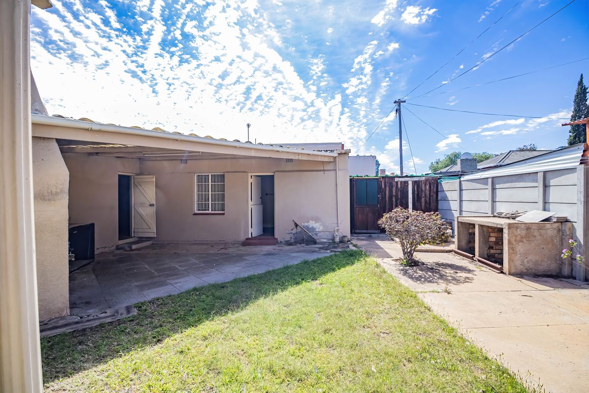 Rear exterior view featuring a covered patio, paved garden area, and a built-in braai structure, offering potential for outdoor entertainment space development.