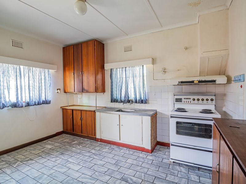 A dated kitchen featuring original cabinetry, a freestanding electric stove, tiled flooring, and a tiled splashback, offering significant potential for a modern renovation.