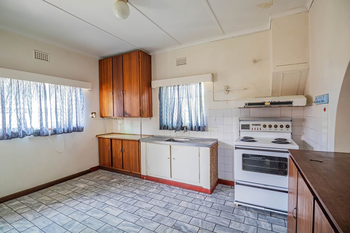 A dated kitchen featuring original cabinetry, a freestanding electric stove, tiled flooring, and a tiled splashback, offering significant potential for a modern renovation.