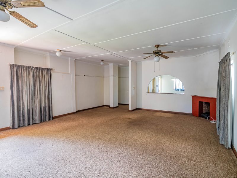 Spacious living room featuring a fireplace, ceiling fans, and an interior archway window, offering a blank canvas for renovation.