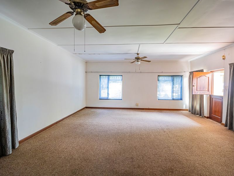 A spacious, empty living room featuring carpet flooring, dual ceiling fans, and direct access to the exterior via a timber door.