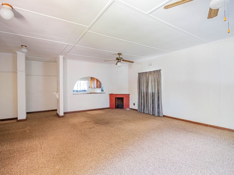 Spacious living area featuring a brick fireplace, ceiling fans, and an arched opening leading to the kitchen area.