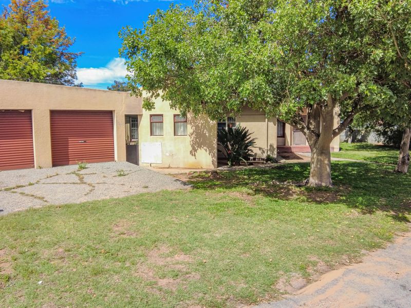 Front exterior view of the house featuring a single garage with a roller door, gravel driveway, and established garden area.