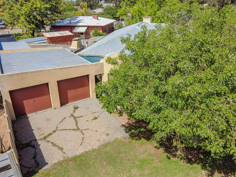 Aerial view of the property showing a double garage with roller doors, a gravel driveway, and a large mature tree in the yard.