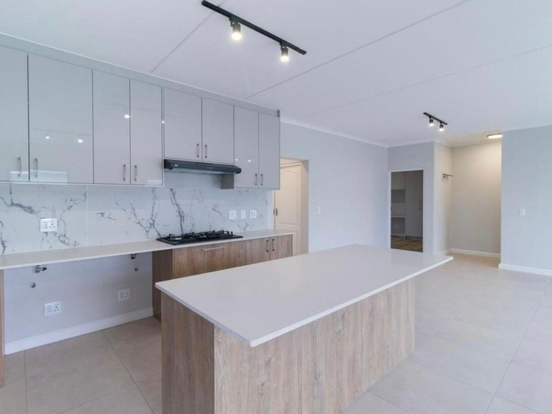 Modern open-plan kitchen featuring sleek cabinetry, stone countertops, a marble-look splashback, gas hob, and a central island, flowing into an airy living space.