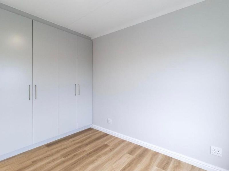 A clean, empty bedroom featuring modern light grey built-in cupboards, neutral walls, and durable laminate wood-look flooring.