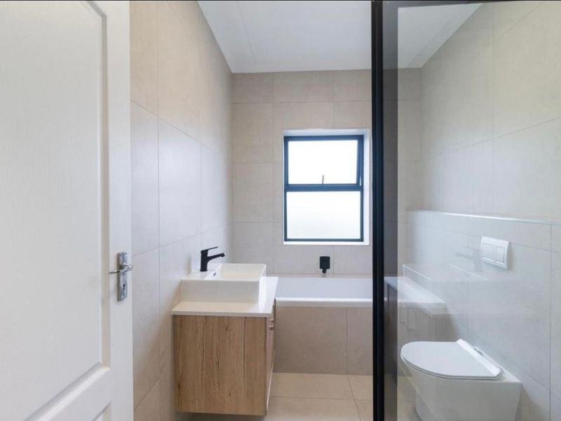 Modern bathroom featuring a wall-mounted vanity, vessel sink, built-in bathtub, wall-hung toilet, and a glass shower screen with contemporary black fixtures.
