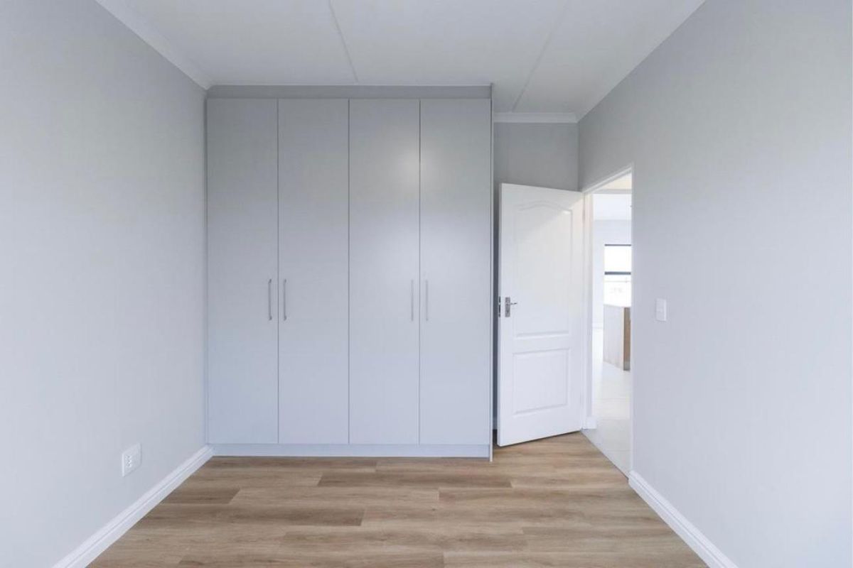 A clean, modern bedroom featuring light grey built-in cupboards, neutral walls, and warm-toned laminate flooring.