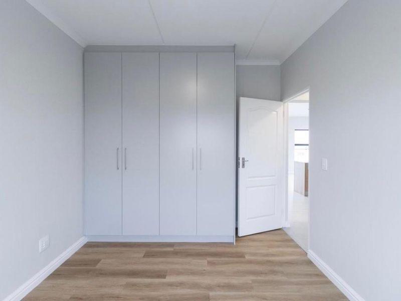 A clean, modern bedroom featuring light grey built-in cupboards, neutral walls, and warm-toned laminate flooring.