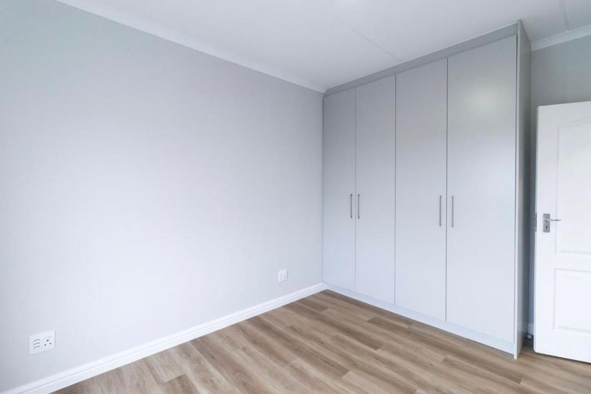 A bright, empty bedroom featuring modern light grey built-in cupboards, neutral walls, and wood-look laminate flooring.