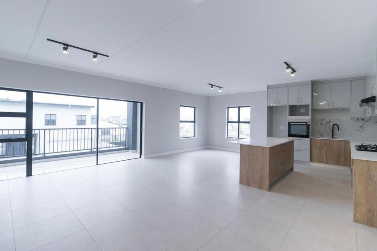 Modern open-plan living area featuring a contemporary kitchen with an island, built-in appliances, and seamless access to a private balcony.