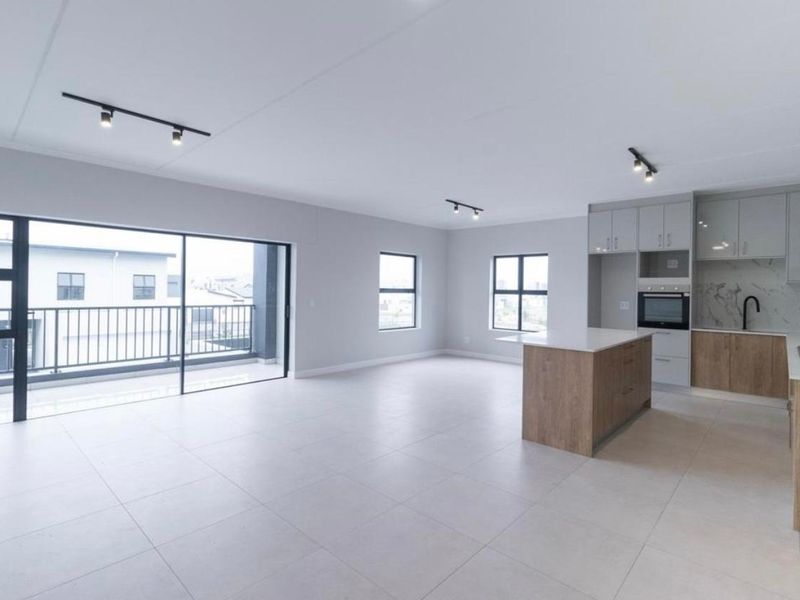Modern open-plan living area featuring a contemporary kitchen with an island, built-in appliances, and seamless access to a private balcony.
