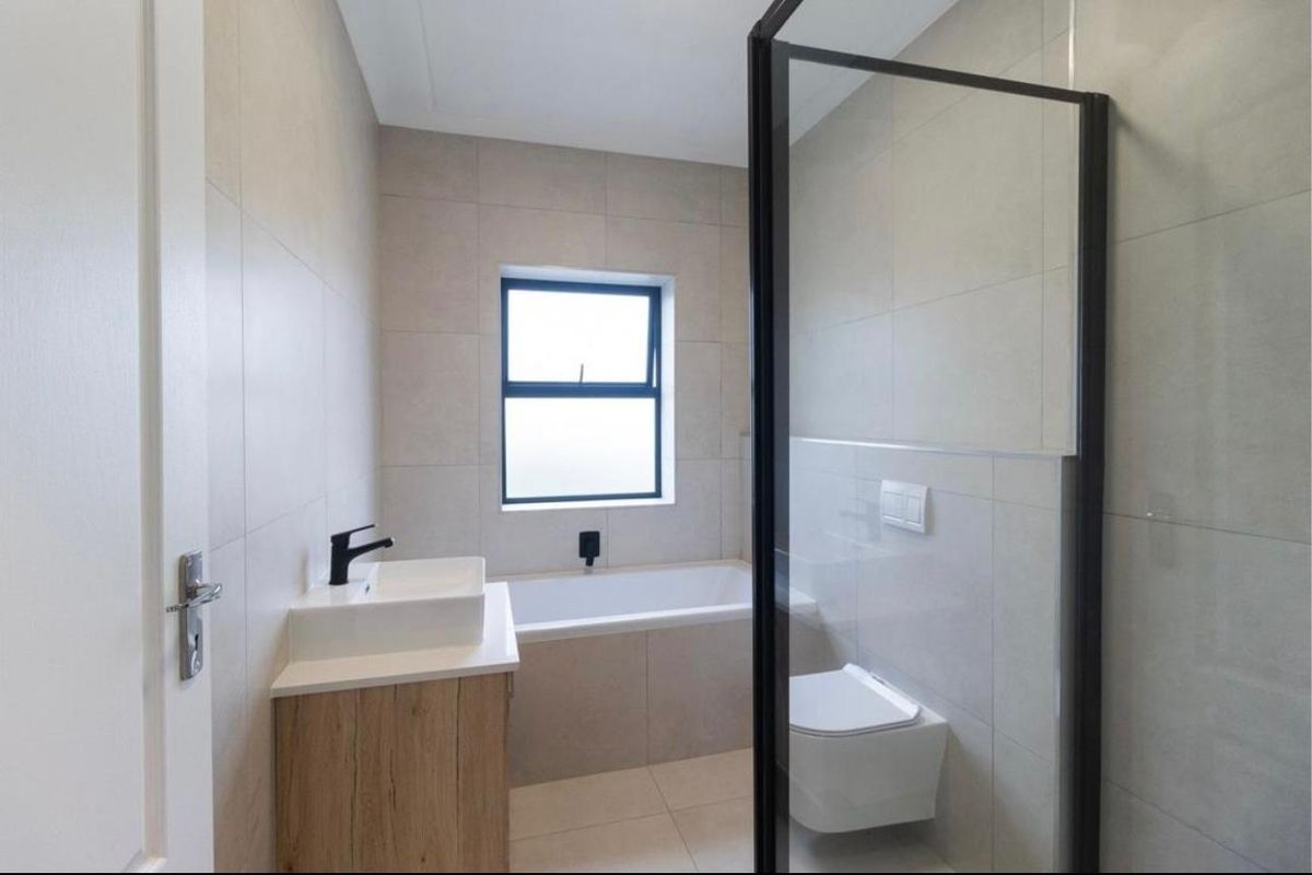 Modern bathroom featuring a built-in vanity, bathtub, wall-mounted toilet, and a glass-enclosed shower with contemporary black fixtures and neutral tiling.