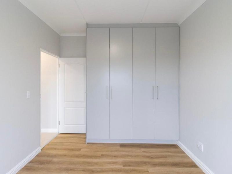 A bright, empty bedroom featuring modern light grey built-in cupboards and durable wood-look laminate flooring.
