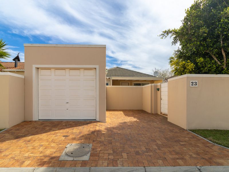Front view of the property featuring a paved driveway, single garage, and secure boundary wall with a pedestrian gate.