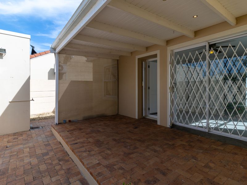 A covered outdoor patio area featuring brick paving, recessed lighting, and a secure sliding glass door entrance to the main living space.