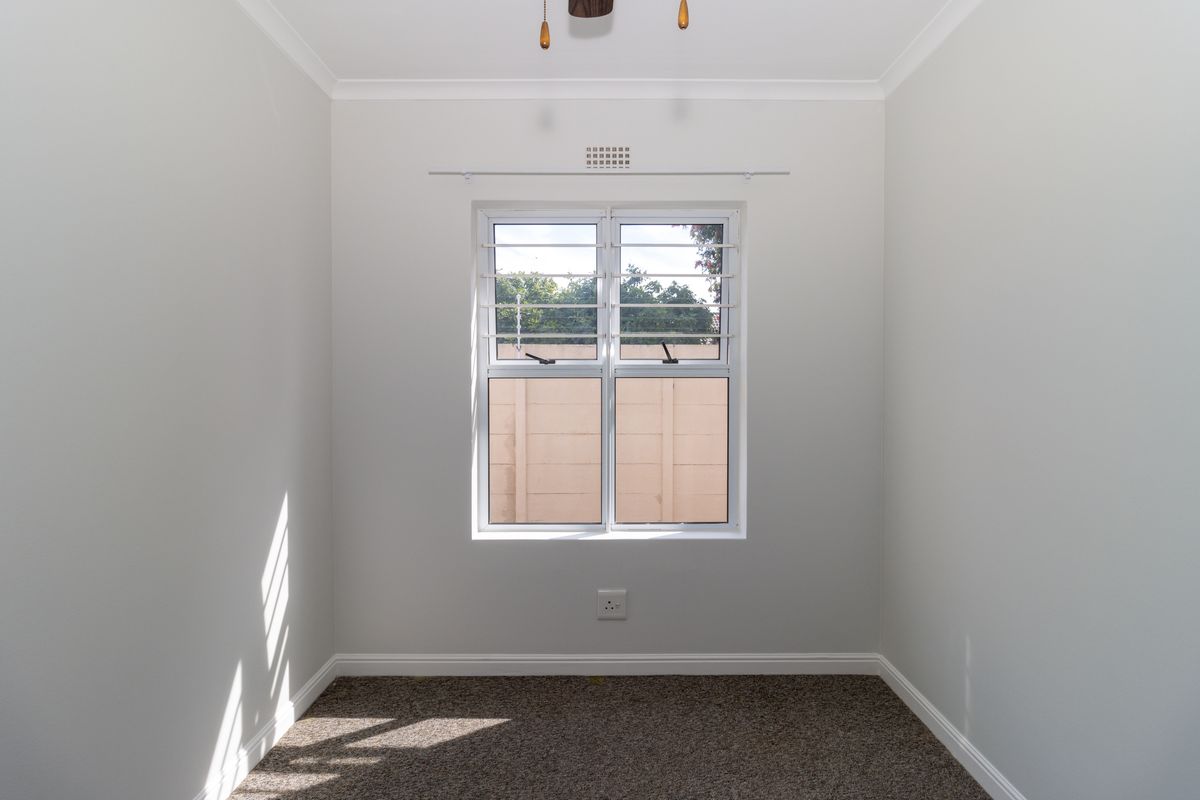 A clean, empty bedroom featuring neutral walls, carpeted flooring, and a window with security bars, providing a blank canvas for personalization.