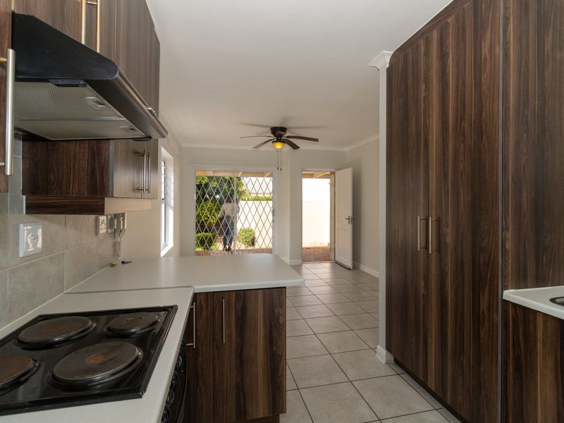 Open plan kitchen featuring dark wood cabinetry, electric hob, and tiled flooring, leading through to an outdoor access area with security gates.