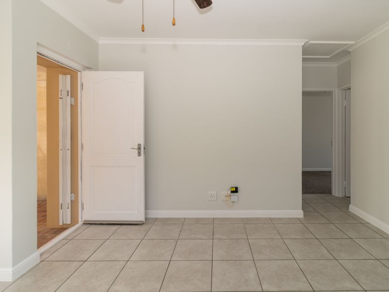 A bright, empty living area featuring neutral tiled flooring, coved cornicing, and a ceiling fan, providing a clean canvas for interior design.