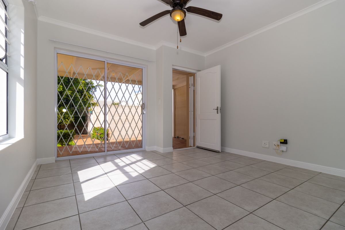 A bright, empty living room featuring neutral tiled flooring, a ceiling fan, and sliding glass doors providing access to the outdoor patio area.