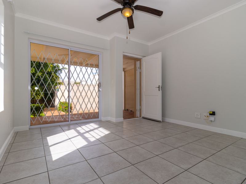 A bright, empty living room featuring neutral tiled flooring, a ceiling fan, and sliding glass doors providing access to the outdoor patio area.