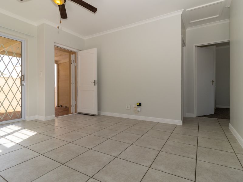 A bright, empty living area featuring neutral tiled flooring, a ceiling fan, and direct access to an outdoor patio through a sliding glass door.