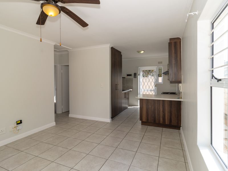 An open-plan living and kitchen area featuring tiled flooring, built-in dark wood cabinetry, and a ceiling fan, offering a clean and functional layout.