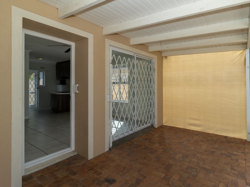 A covered patio area featuring brick paving, timber ceiling beams, and secure sliding door access to the interior living space.