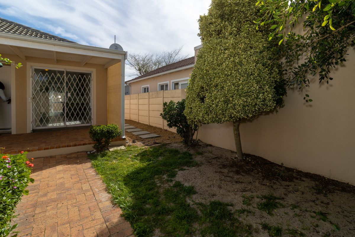 Rear exterior view featuring a brick paved patio, sliding glass door with security gate, and a precast concrete boundary wall with garden area.