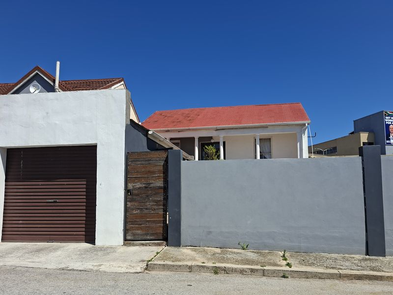 Front elevation of a residential property featuring a roller garage door, a timber pedestrian gate, and a perimeter wall with a corrugated metal roof.