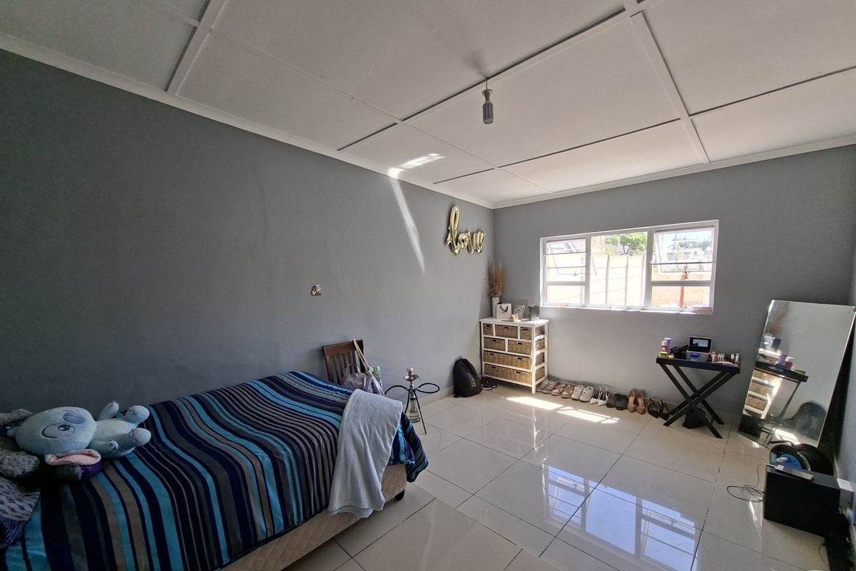 A bedroom featuring tiled flooring, neutral grey walls, and natural light from an aluminium-framed window.