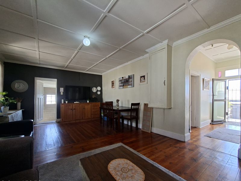 Spacious living area featuring original hardwood flooring, a distinctive coffered ceiling, and a classic architectural archway leading to the entrance.