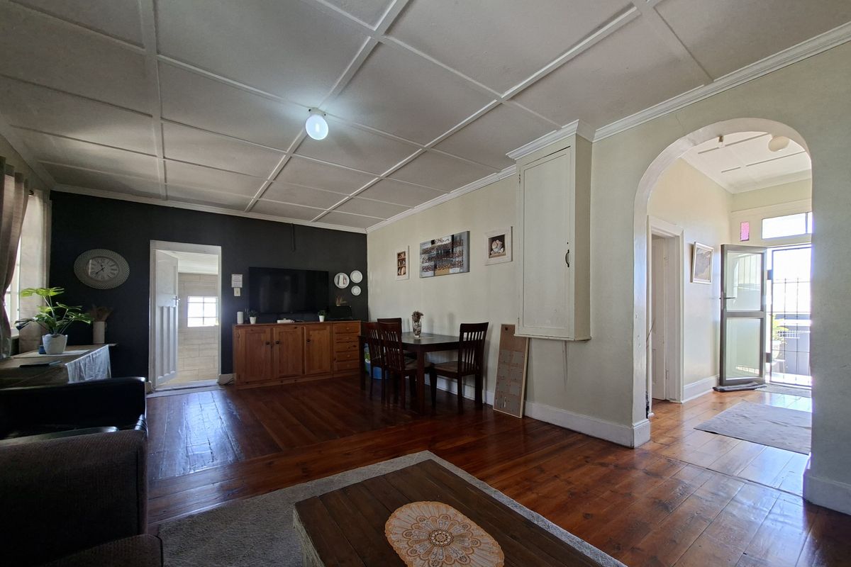 Spacious living area featuring original hardwood flooring, a distinctive coffered ceiling, and a classic architectural archway leading to the entrance.