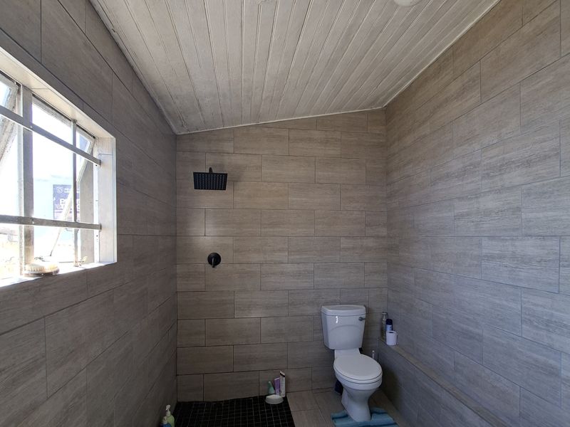 A functional bathroom featuring wood-look wall tiles, a walk-in shower area, a standard toilet, and a timber-clad ceiling with surface-mounted lighting.