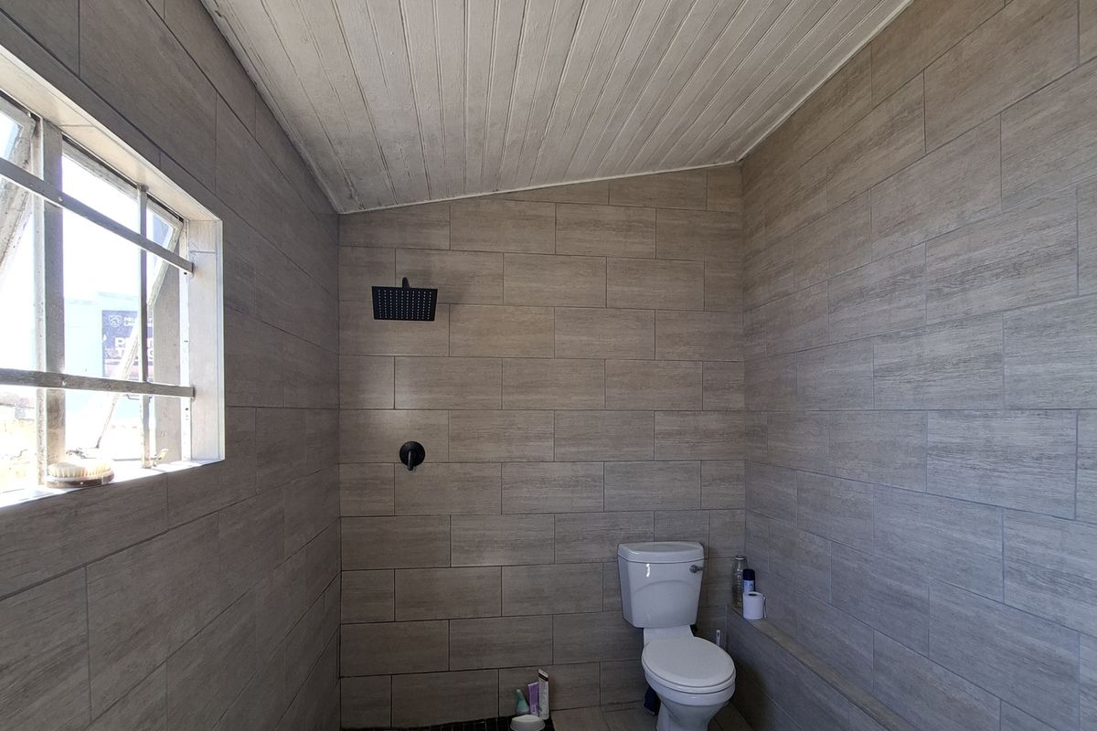 A functional bathroom featuring wood-look wall tiles, a walk-in shower area, a standard toilet, and a timber-clad ceiling with surface-mounted lighting.
