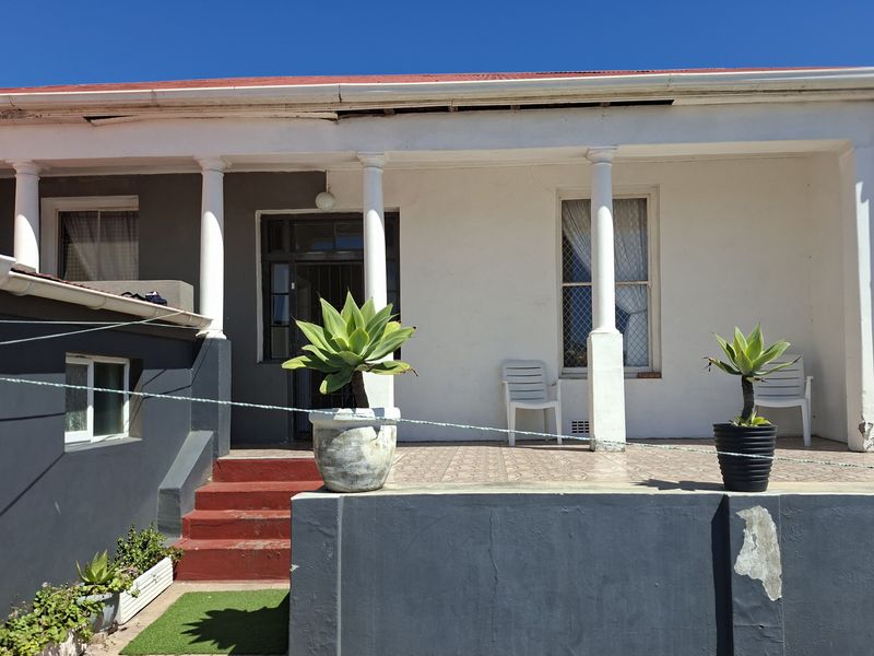 A covered front patio area featuring concrete columns and tiled flooring, showing signs of exterior wear and maintenance requirements.