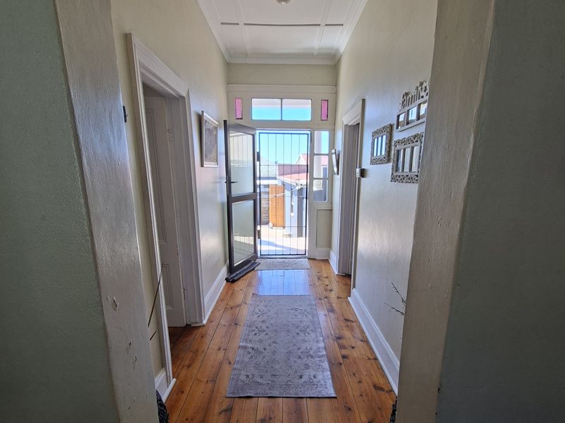 A bright hallway featuring original hardwood flooring, a classic archway, and a secure entrance door with a transom window.