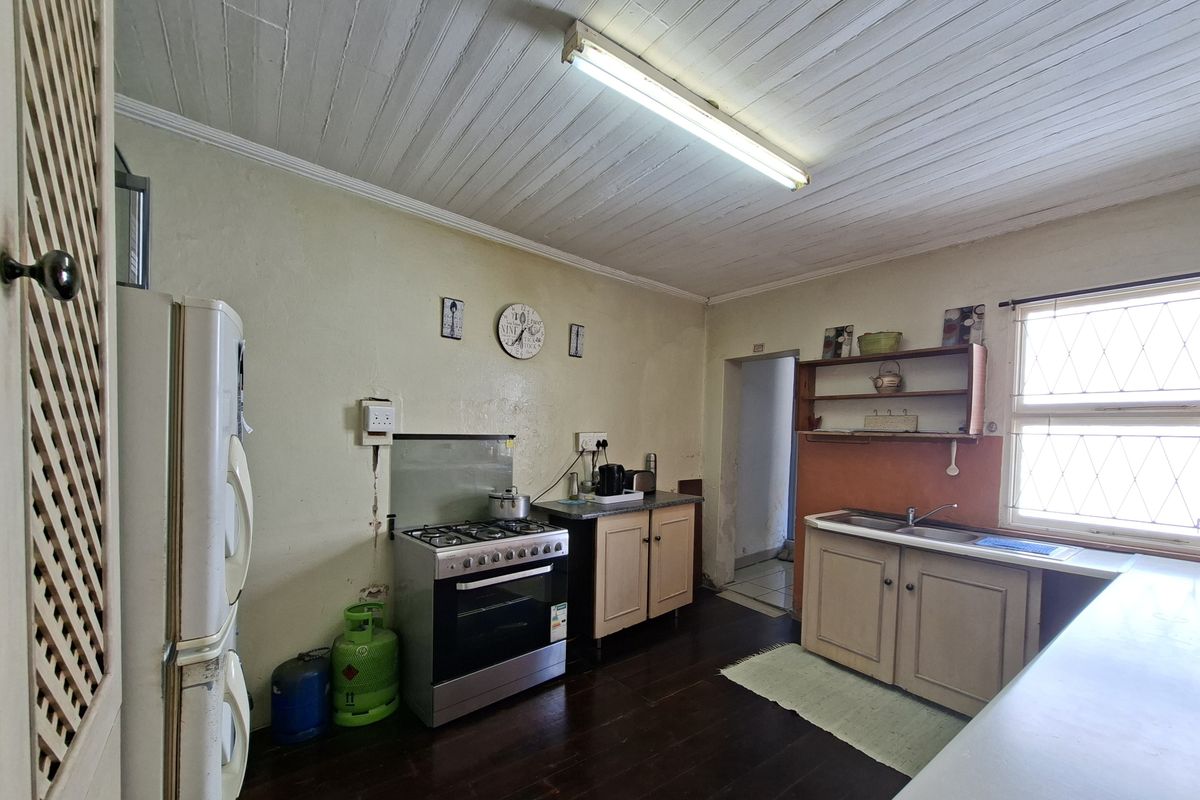 A functional kitchen featuring timber ceilings, gas stove, built-in cabinetry, and a stainless steel sink, requiring cosmetic updates to modernize the space.