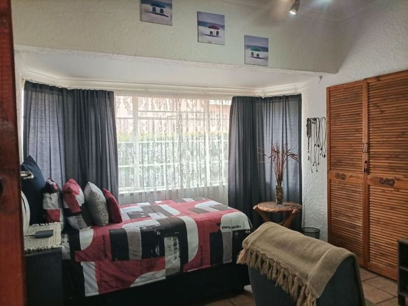 A bedroom featuring built-in wooden louvered wardrobes, tiled flooring, and a large window with security bars, providing natural light.