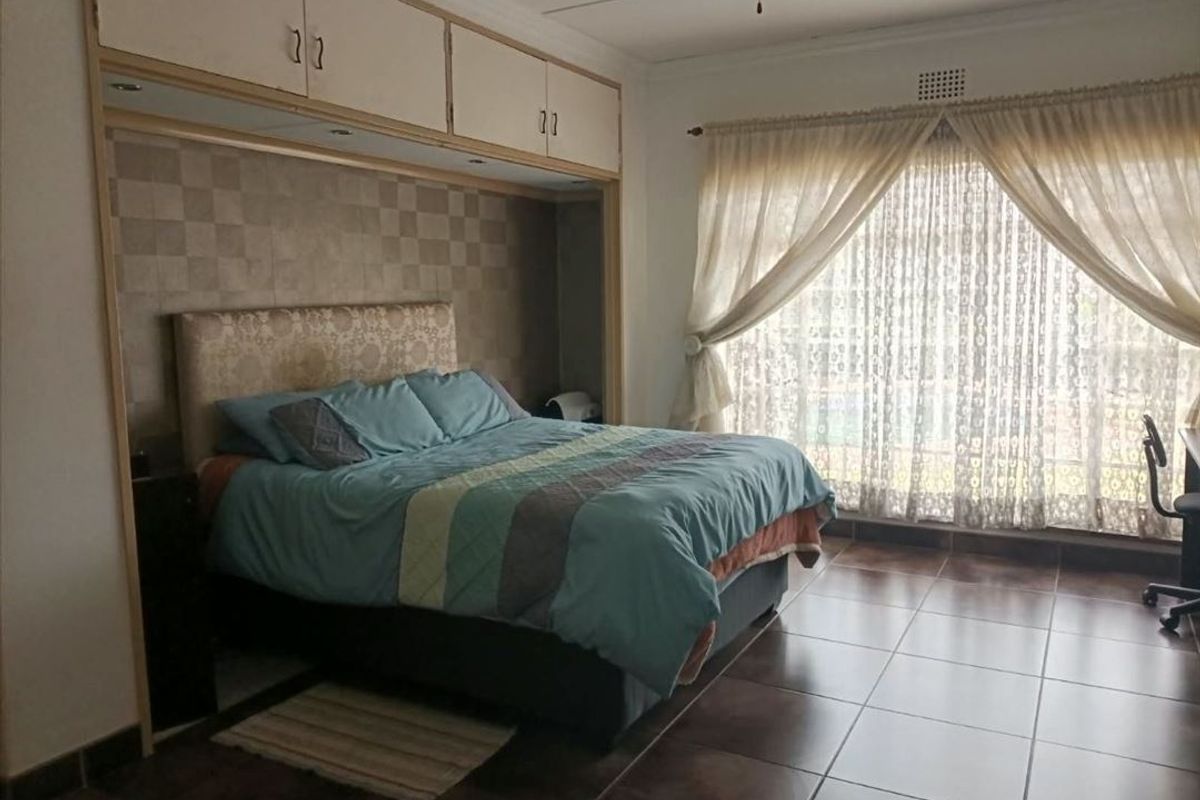 Spacious bedroom featuring built-in overhead cabinetry, large tiled flooring, and natural light through window curtains.