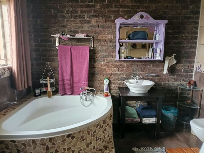 A bathroom featuring a corner bathtub with a stone-tiled surround, a vessel sink on a vanity stand, and an exposed brick feature wall.